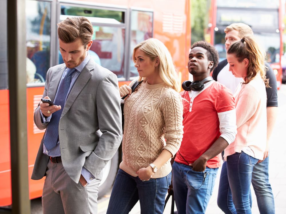 Pessoas esperando ônibus em fila única, cenário comum que reflete diferentes tipos de fila de espera em espaços públicos urbanos.